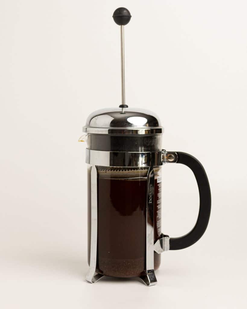 French press with top on, with filter pressed down to touch water