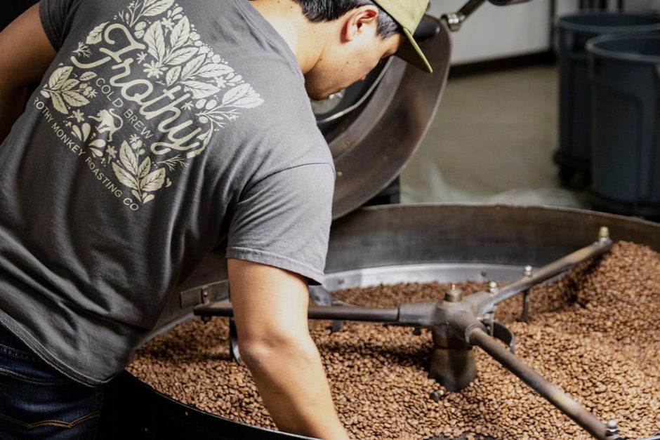 view of coffee roaster from behind with their hands in freshly roaster coffee beans. 