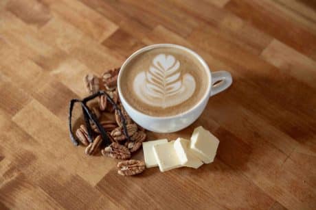 "Like Butta" fall and winter seasonal latte on a table with some ingredients including butter, pecans and vanilla bean pods. 